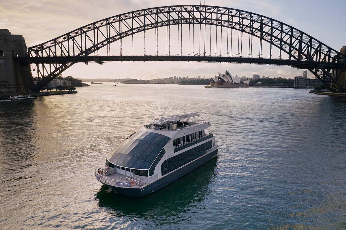 The Clearview glass cruise vessel under the Sydney Harbour Bridge with the Opera House behind